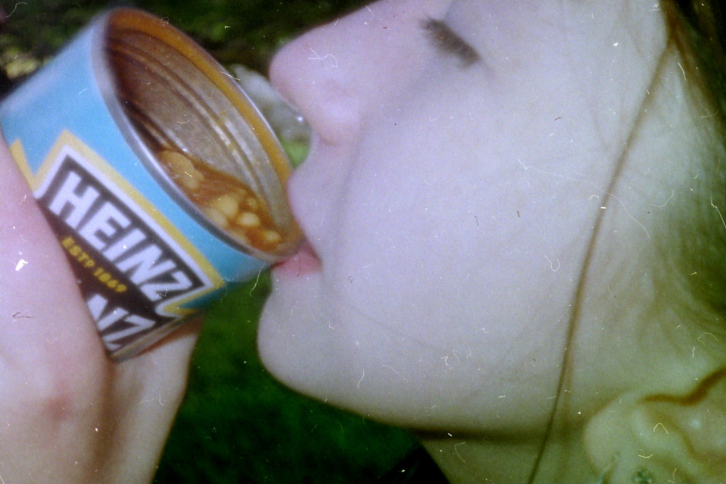 person drinking from a can of baked beans
